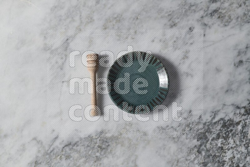 Multicolored pottery plate with wooden honey dipper on the side on grey marble background
