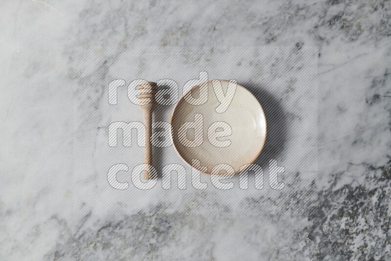 Beige pottery plate with wooden honey dipper on the side on grey marble background