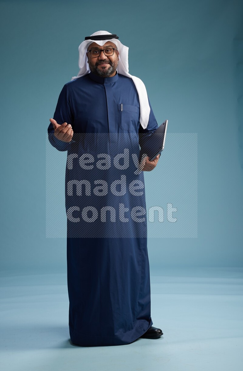 Saudi Man with shimag Standing working on laptop on blue background
