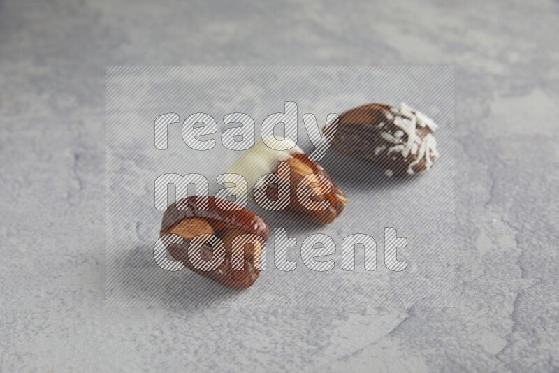 Three Almond stuffed dates plain and covered with chocolate on a light grey background