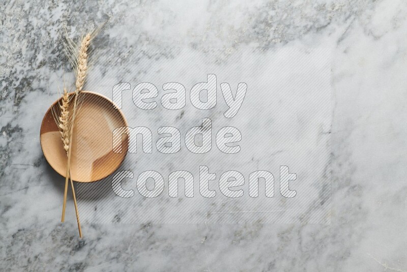 Wheat stalks on multicolored pottery plate on grey marble background