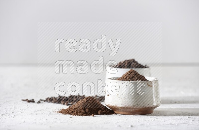 وعاءين من السيراميك بيج اللون، أحدهما مملوء بالقرنفل والآخر مملوء بالبودرة على أرضية بيضاء