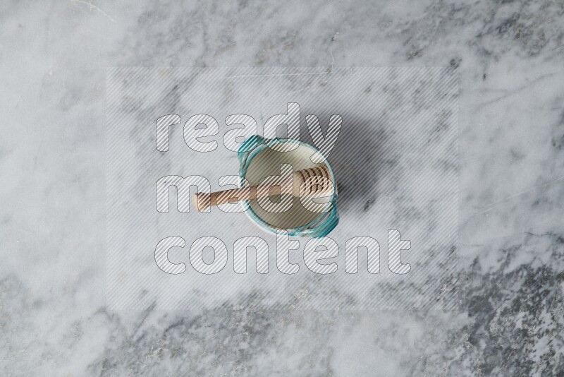 Multicolored pottery bowl with wooden honey dipper in it on grey marble background