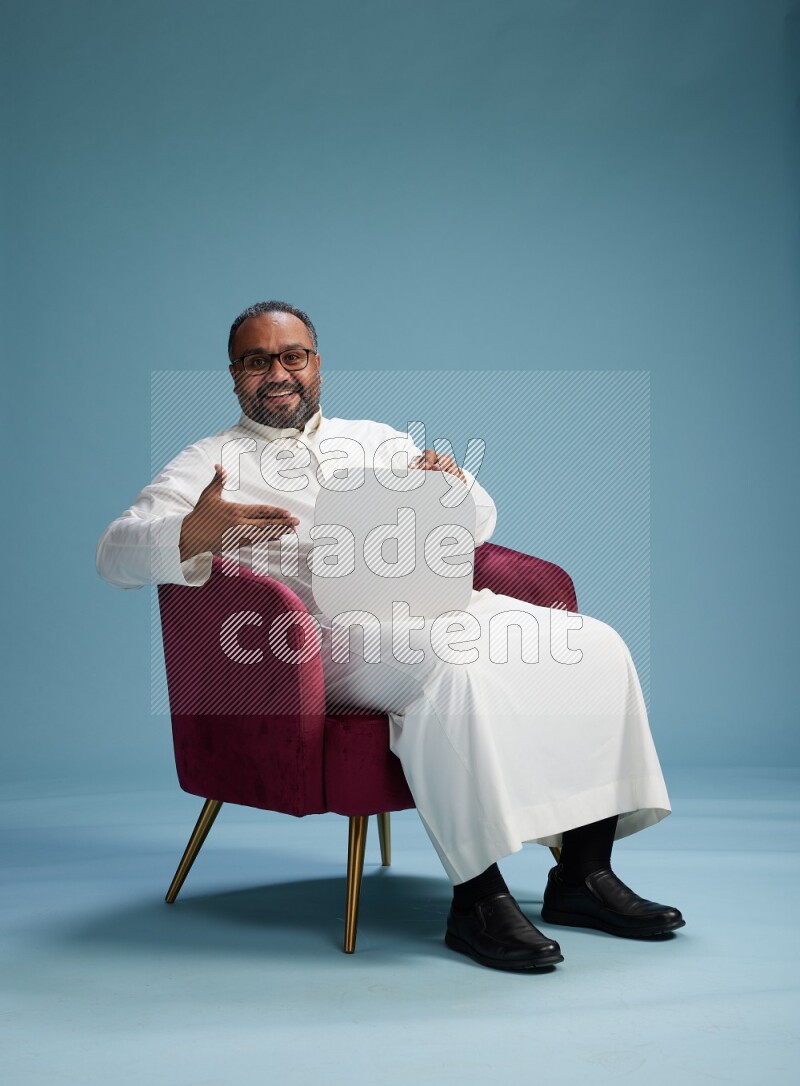 Saudi Man without shimag sitting on chair holding social media sign on blue background