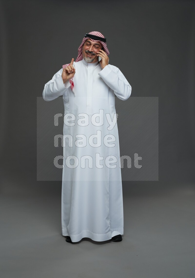 Saudi man with shomag Standing talking on phone on gray background