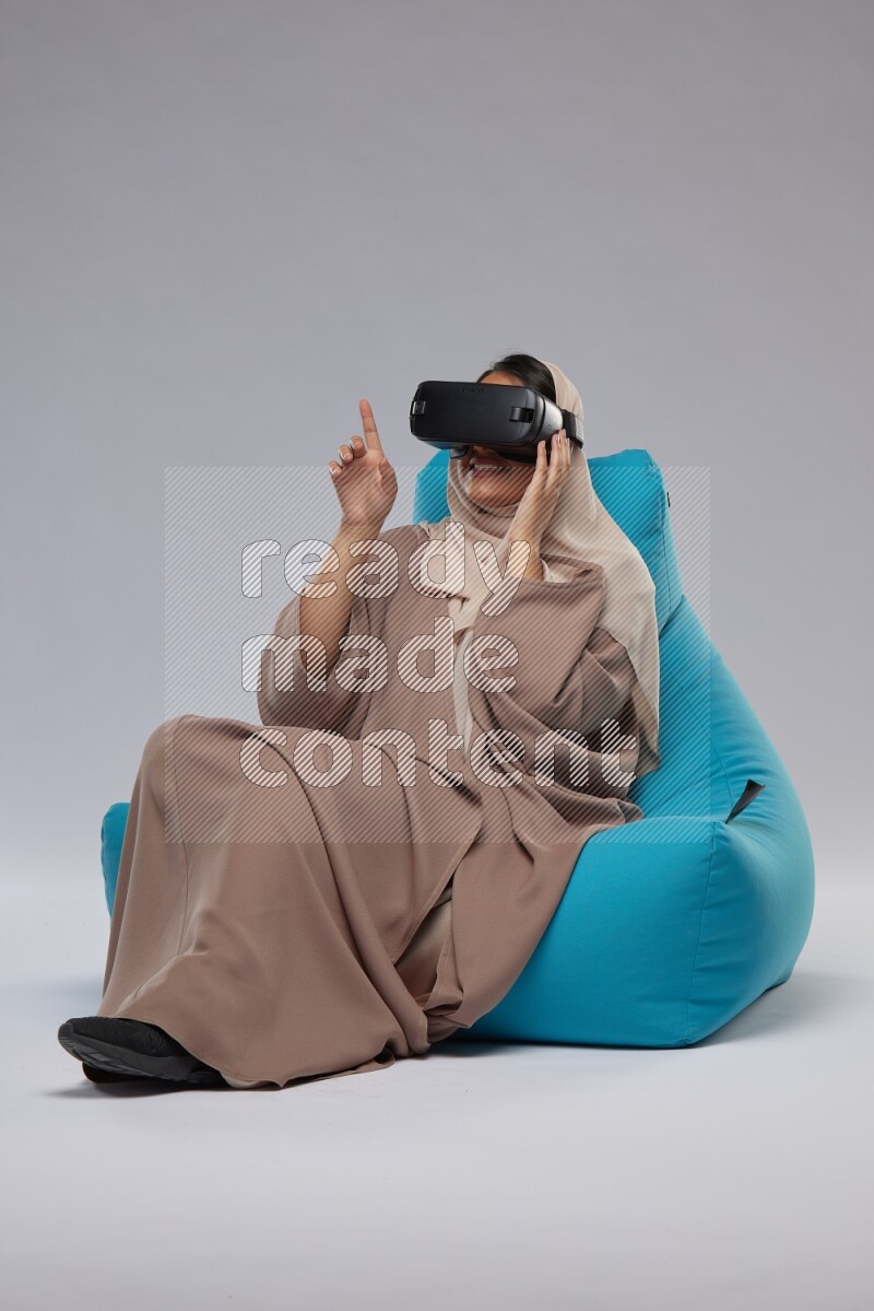 A Saudi woman sitting on a blue beanbag and gaming with VR