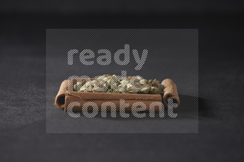 أربعة من أعواد القرفة مكونة شكل مربع بداخلها حبوب الهيل علي خلفية سوداء