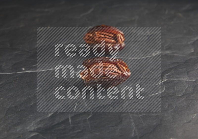 two pecan stuffed madjoul dates on a black textured background