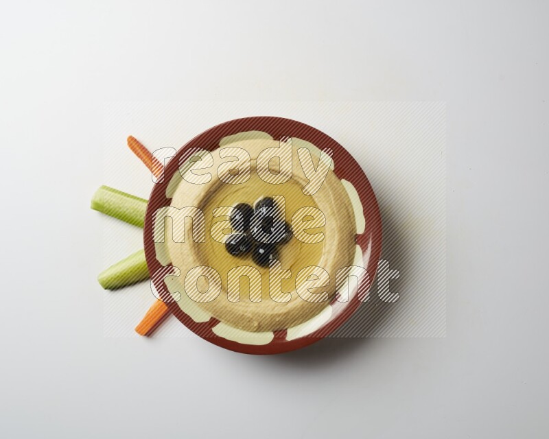 Hummus in a traditional plate garnished with black olives on a white background