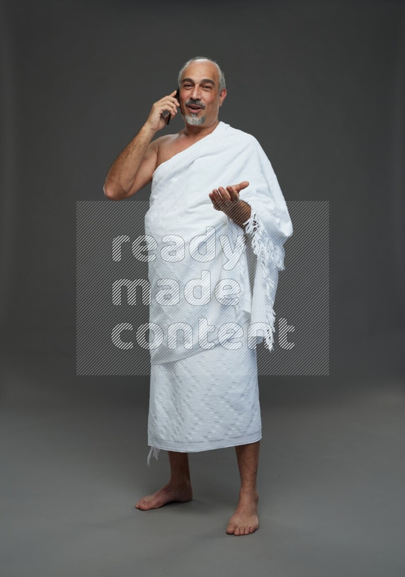 A man wearing Ehram Standing talking on phone on gray background