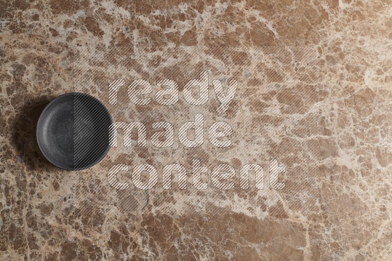 A black pottery bowl on beige marble background