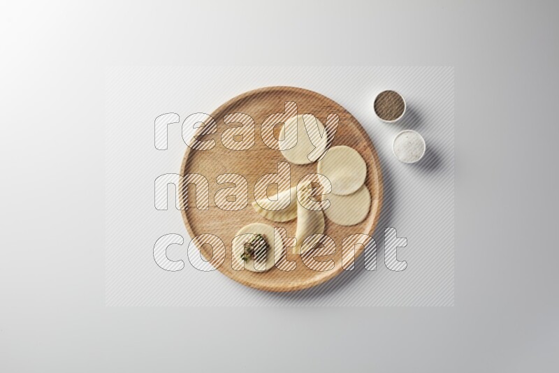 two closed sambosas and one open sambosa filled with meat while salt and black pepper aside in a wooden dish on a white background