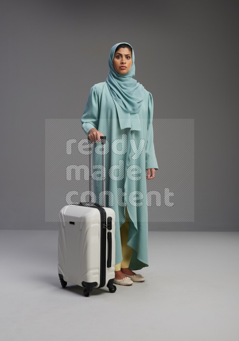 Saudi Woman wearing Abaya standing holding Travel bag on Gray background