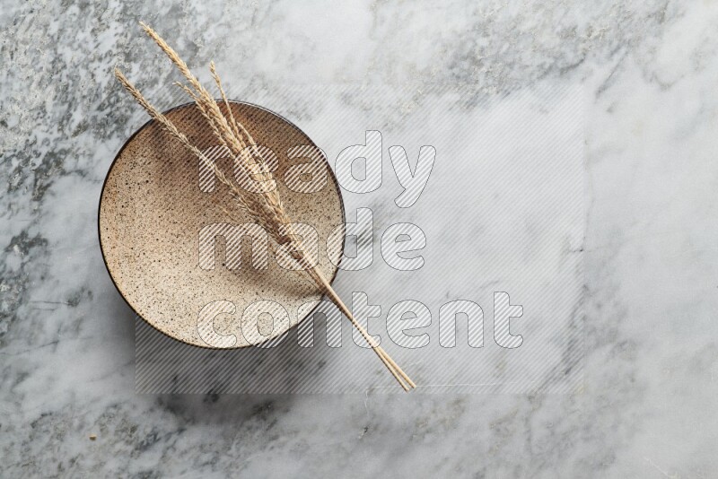 Wheat stalks on multicolored pottery plate on grey marble background