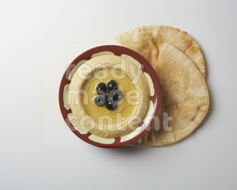 Hummus in a traditional plate garnished with black olives on a white background