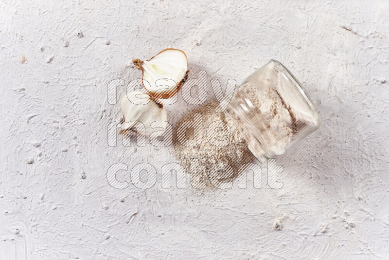 A glass jar full of onion powder flipped with some spilling powder on white background