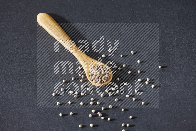 A wooden spoon full of white pepper beads on black flooring