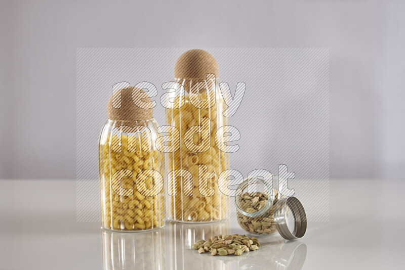 Raw pasta in glass jars with cardamom on light grey background