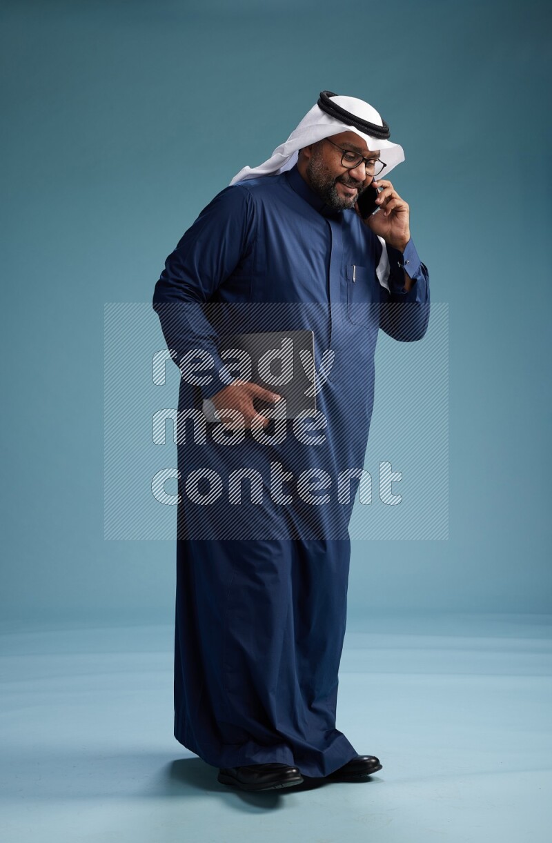 Saudi Man with shimag Standing talking on phone on blue background