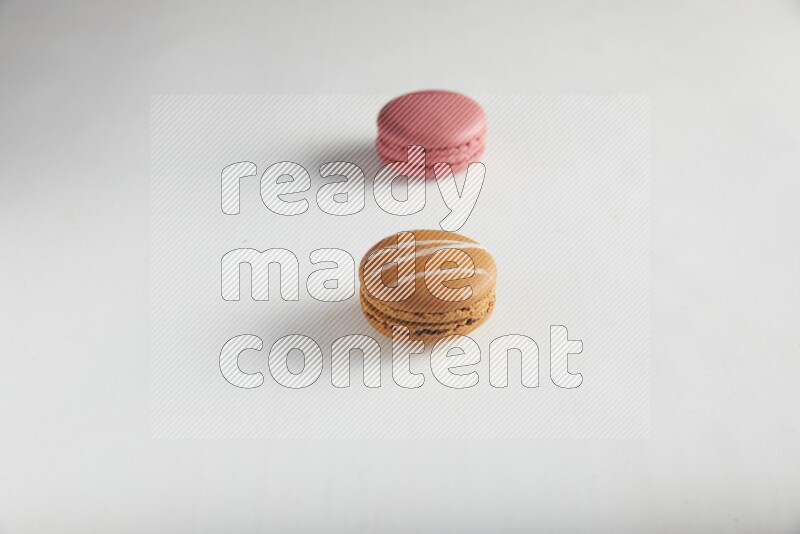 45º Shot of of two assorted Brown Irish Cream, and Pink Raspberry macarons on white background