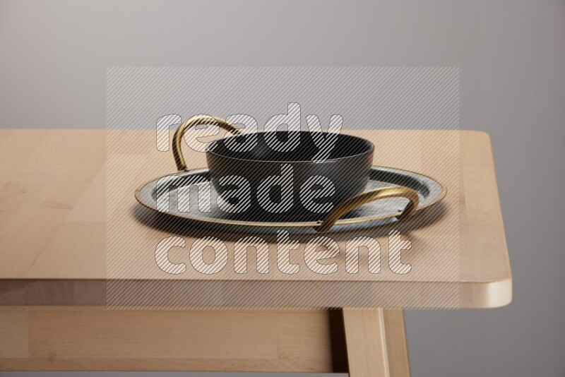black bowl placed on a rounded stainless steel tray with golden handels on the edge of wooden table