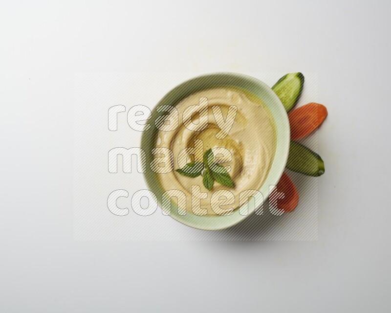 Hummus in a green plate garnished with mint on a white background