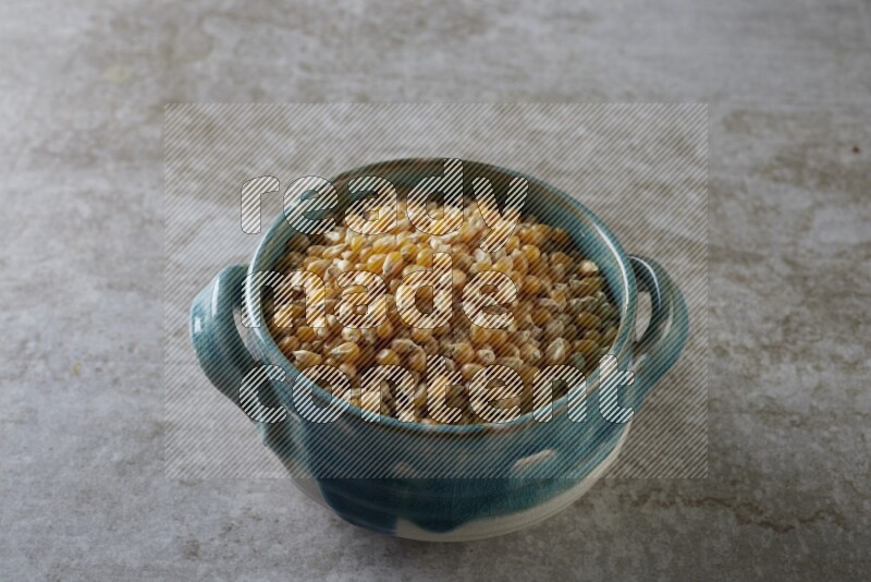 corn kernel in a multi-colored handheld ceramic bowl on a grey textured countertop