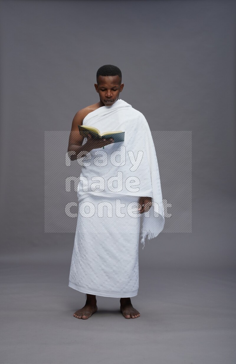 A man wearing Ehram Standing reading quran on gray background