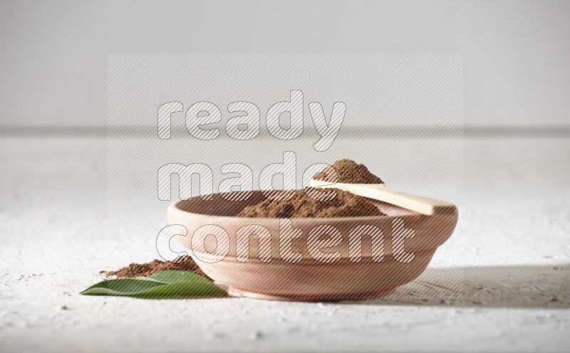 A wooden bowl and a wooden spoon full of cloves powder on a textured white flooring