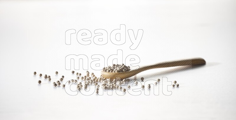 ملعقة خشبية مملوءة بحبوب الفلفل الأبيض على أرضية بيضاء