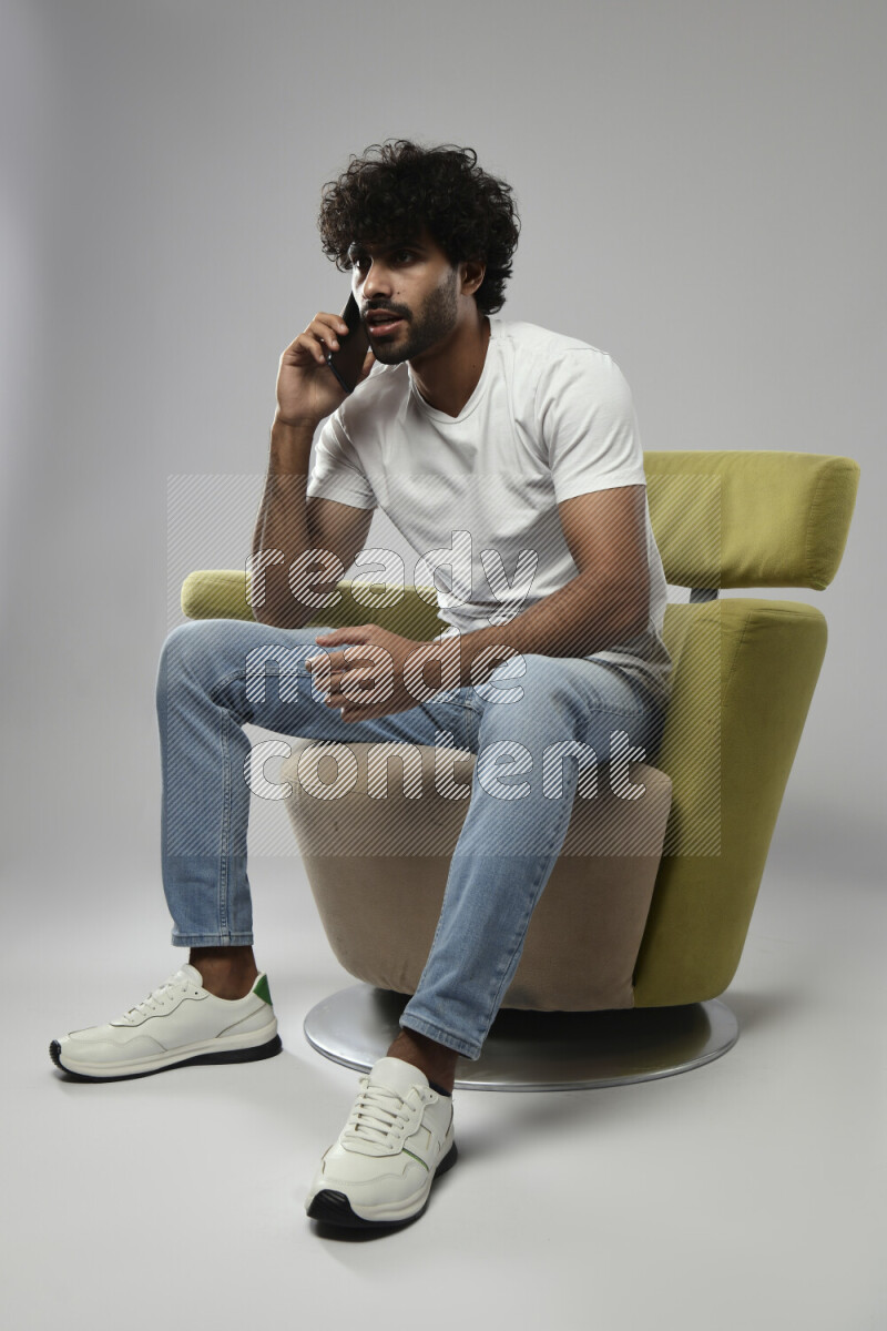 A man wearing casual sitting on a chair talking on the phone on white background