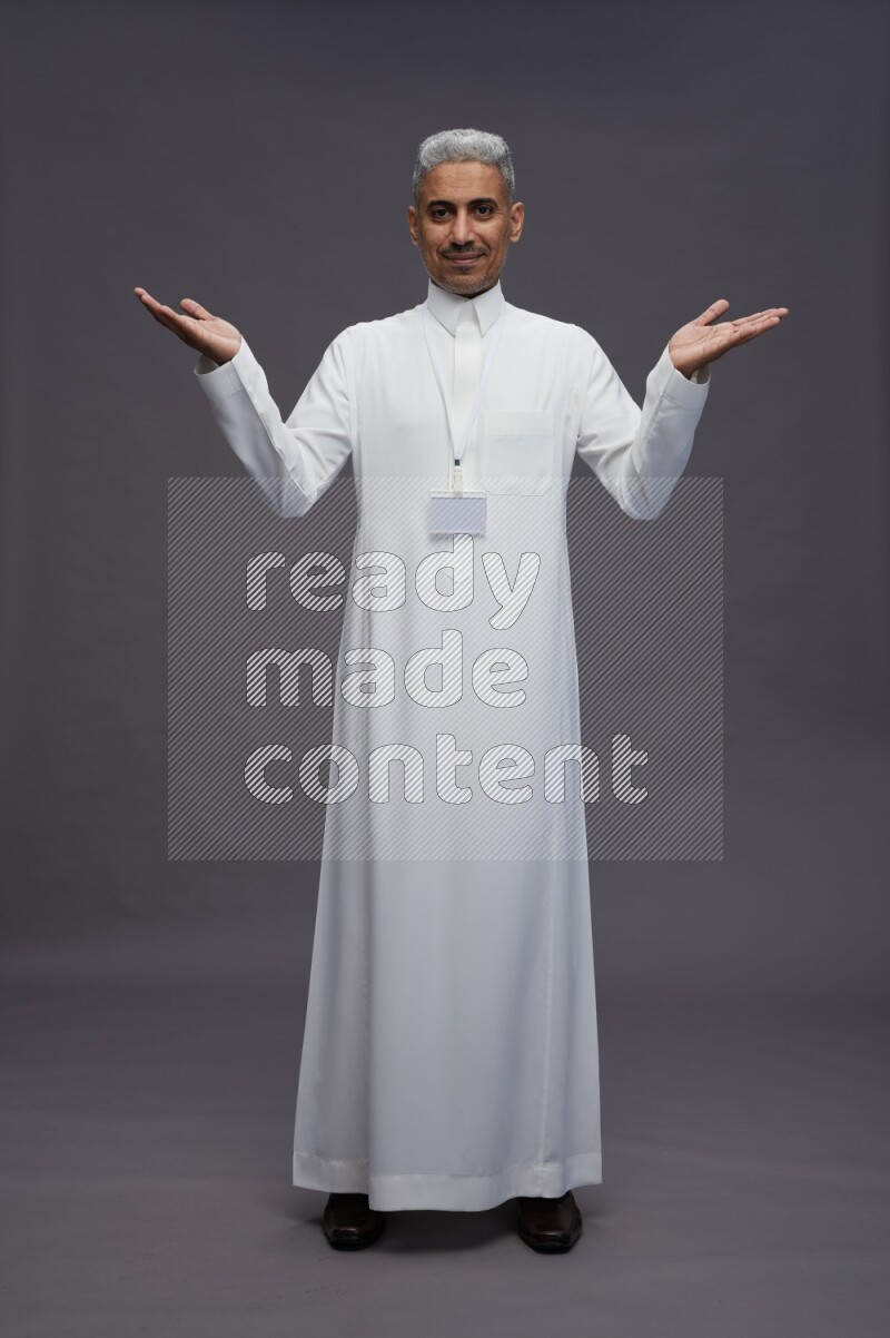 Saudi man wearing thob with neck strap employee badge standing interacting with the camera on gray background