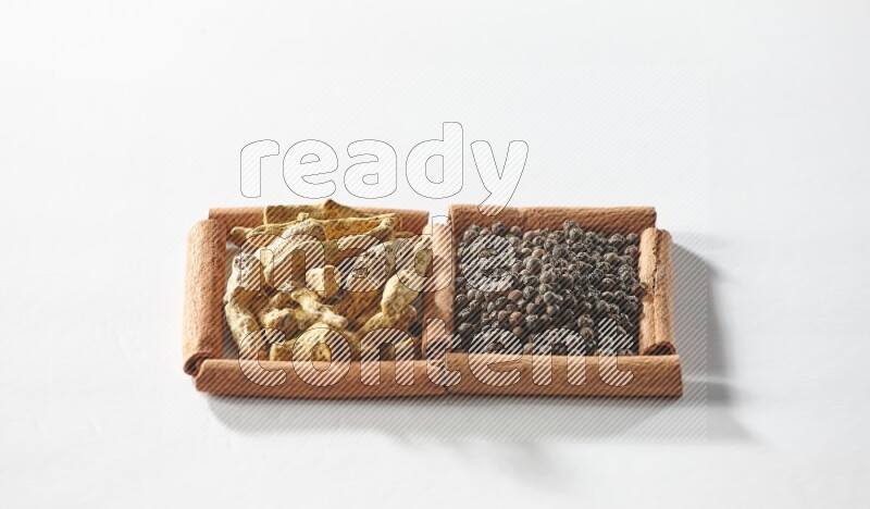 مربعان من أعواد القرفة ممتلئان بحبوب الفلفل الأسود وأصابع الكركم علي خلفية بيضاء