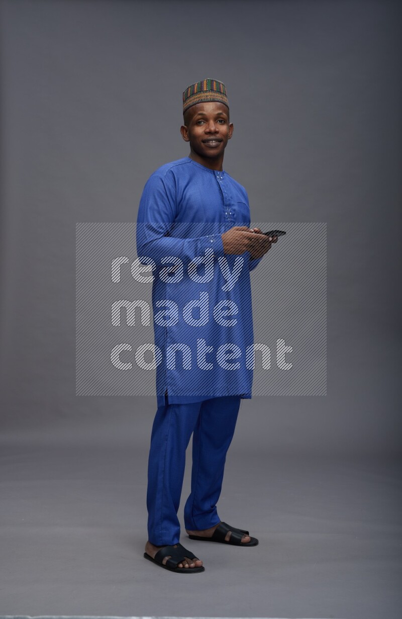 Man wearing Nigerian outfit standing texting on phone on gray background