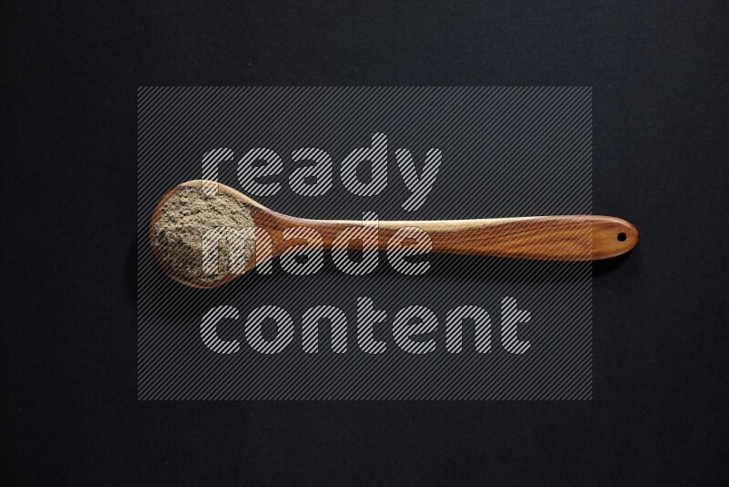 A wooden ladle full of cardamom powder on black flooring