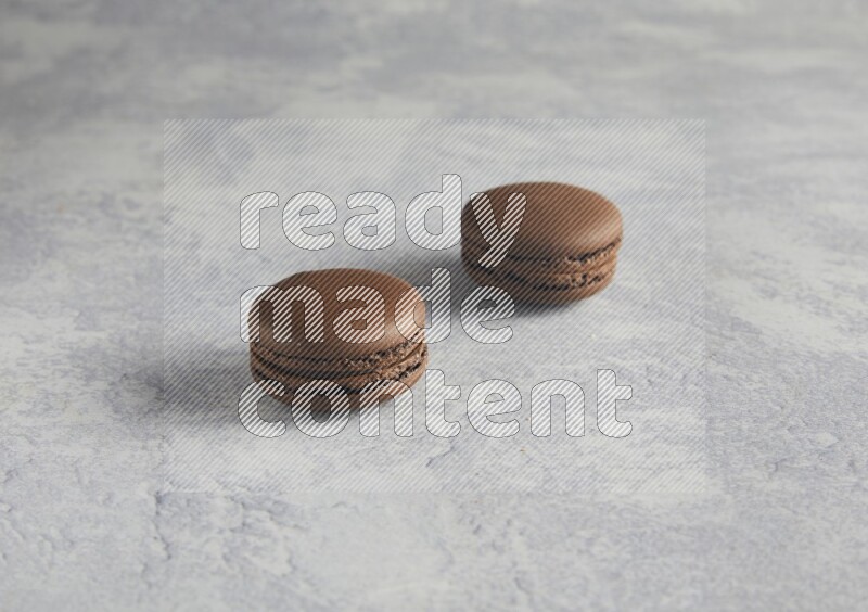 45º Shot of two Brown Dark Chocolate macarons  on white  marble background