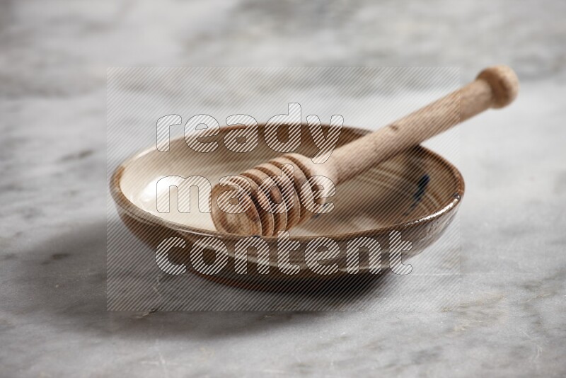 Multicolored pottery bowl with wooden honey dipper in it on grey marble background