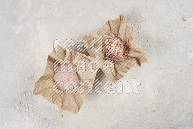 A crumpled piece of paper full of pink himalayan salt on white background