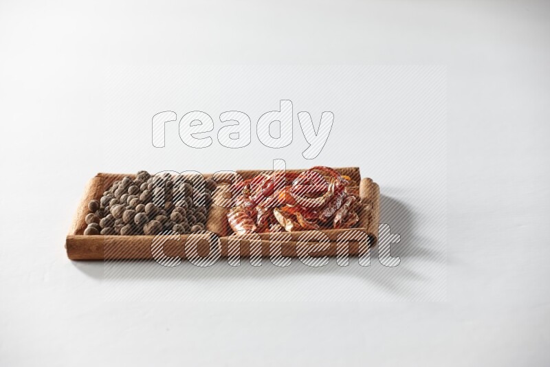 مربعان من أعواد القرفة ممتلئان بالفلفل الحار المجفف وحبوب بهار الفلفل الحلو علي خلفية بيضاء