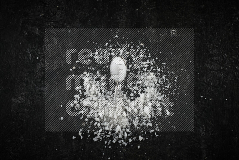 2 metal spoons filled with white salt on black background