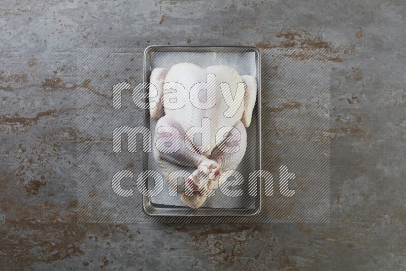 whole Raw chicken on a small oven trey direct on a rustic grey background