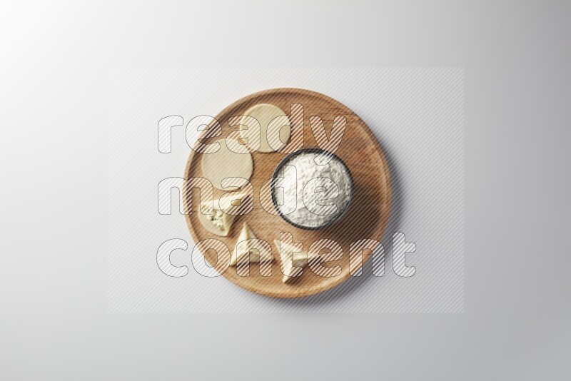 two closed sambosas and one open sambosa filled with cheese while flour aside in a wooden dish on a white background
