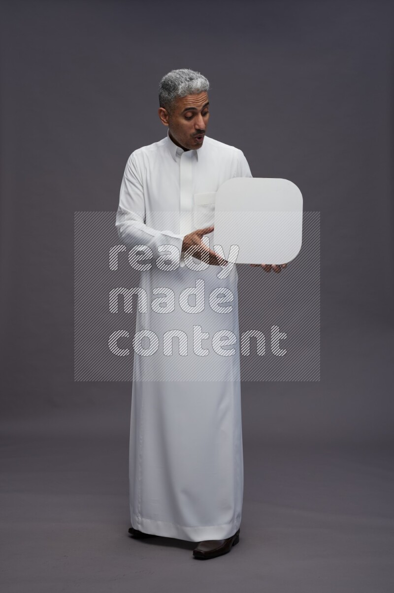 Saudi man wearing thob standing holding social media sign on gray background