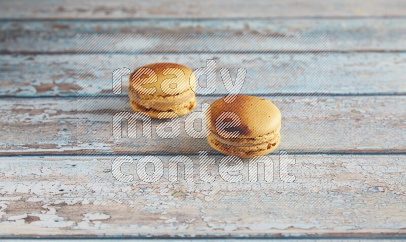 45º Shot of two Yellow Crème Brulée macarons on light blue wooden background