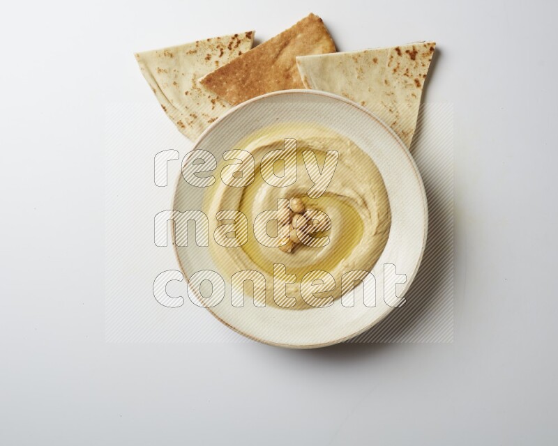 Hummus in a pottry plate garnished with roasted chickpeas on a white background