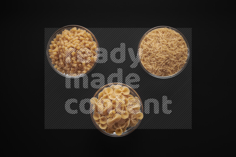 Different pasta types in glass bowls on black background