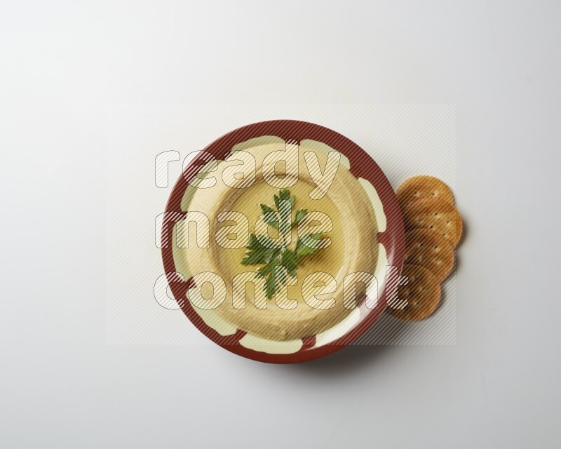 Hummus in a traditional plate garnished with parsley on a white background