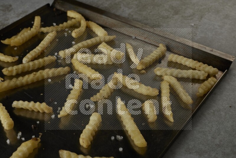 crinkle fries in a black stainless steel rectangle tray on grey textured counter top
