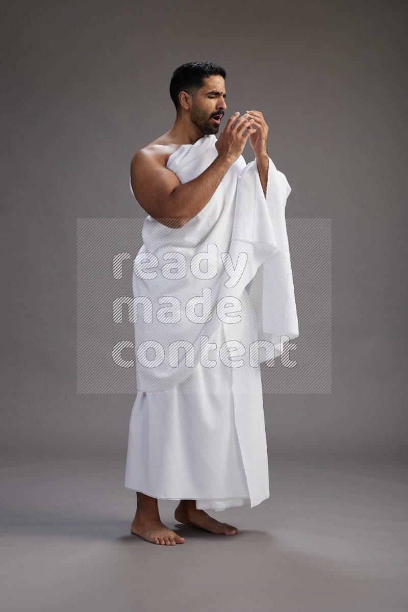 A man wearing Ehram standing showing how to sneeze on gray background
