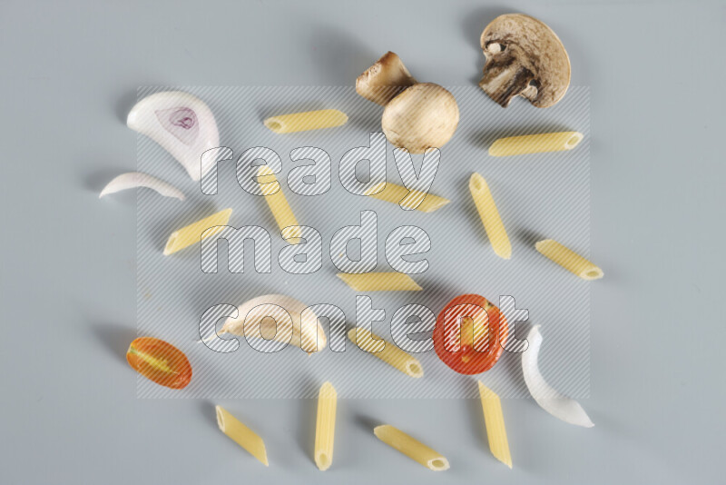 Raw pasta with different ingredients such as cherry tomatoes, garlic, onions, red chilis, black pepper, white pepper, bay laurel leaves, rosemary, cardamom and mushrooms on light blue background